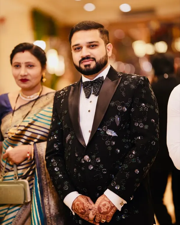 A client looking dapper in a custom black tuxedo. The jacket is adorned with intricate cut dana beadwork in black, green, and blue, creating a glittering, designer feel perfect for a reception.