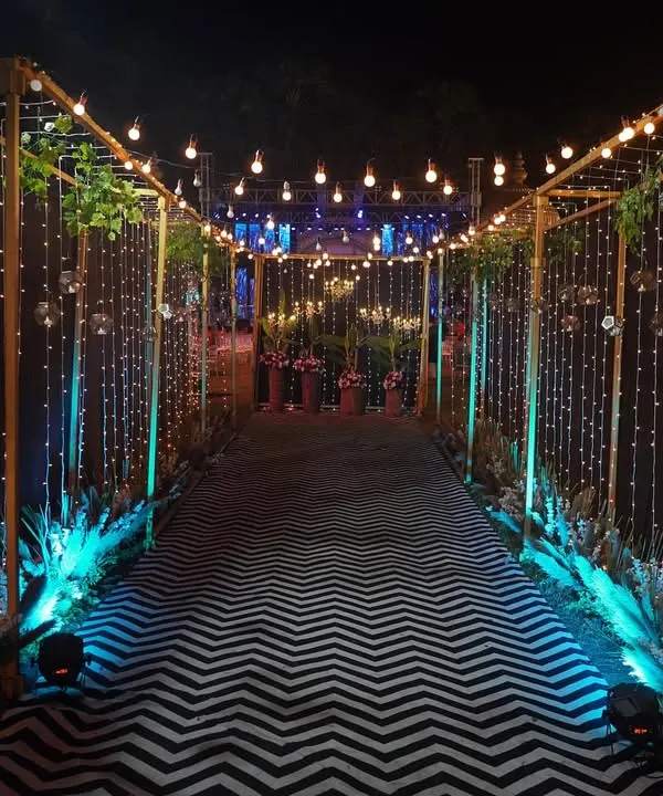 A mesmerizing entranceway for an evening event. The passage is lined with golden frames wrapped in fairy lights, with a modern chevron pattern carpet leading guests into the venue.