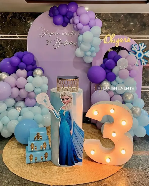A magical Frozen-themed party for Dhiyara's 3rd birthday, featuring an Elsa cutout, a purple and blue balloon cascade, and a light-up marquee number.