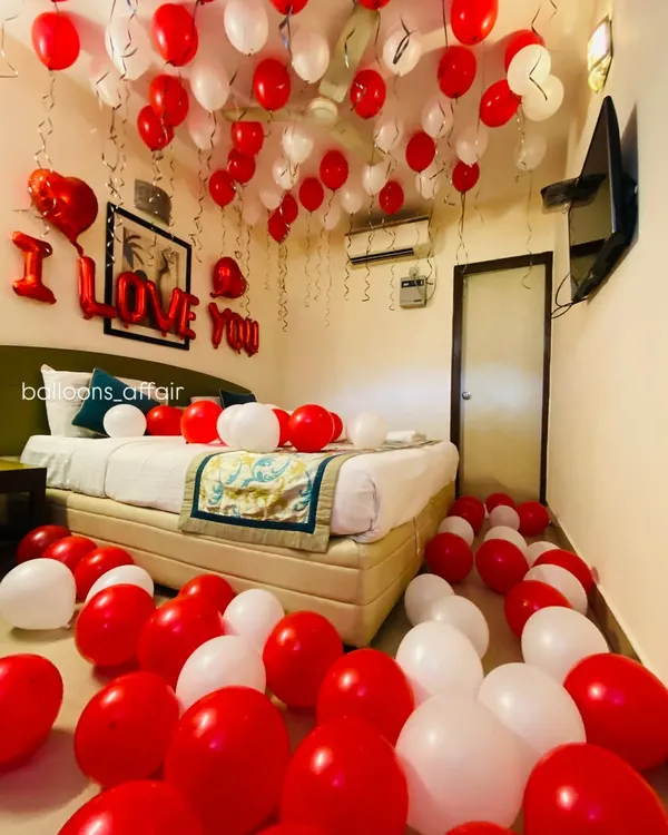 The quintessential romantic room setup. This hotel room is filled with red and white balloons on the floor and ceiling, with a bold "I LOVE YOU" message above the bed.