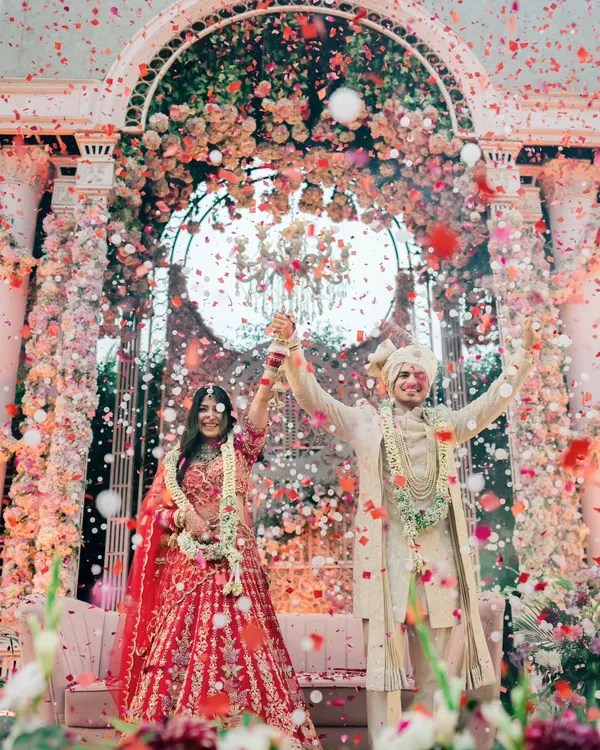 A moment of pure triumph and celebration. As confetti rains down, the couple raises their hands, united and joyful, under a magnificent floral mandap.