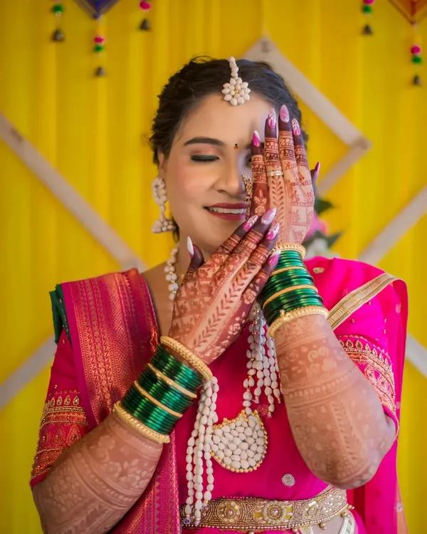 A shy and beautiful smile from a bride during her wedding ceremony. Her hands, adorned with intricate henna and green bangles, frame her face, highlighting the traditional details and her joyful expression.