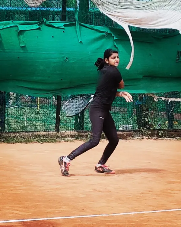 A junior girl hits a focused backhand during an AITA U-14 tournament match, demonstrating proper form and concentration.