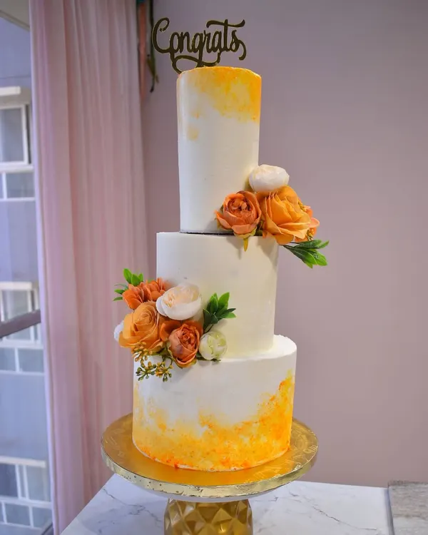 A stunning three-tiered wedding cake with a warm orange watercolor effect and delicate floral arrangements. This design combines modern artistry with timeless elegance for a truly special day.