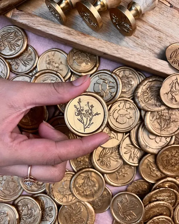 A close-up of one of our handmade gold wax seals, featuring a delicate botanical design. We offer a variety of floral and nature-inspired stamps to add a personal and artisanal touch to your stationery.