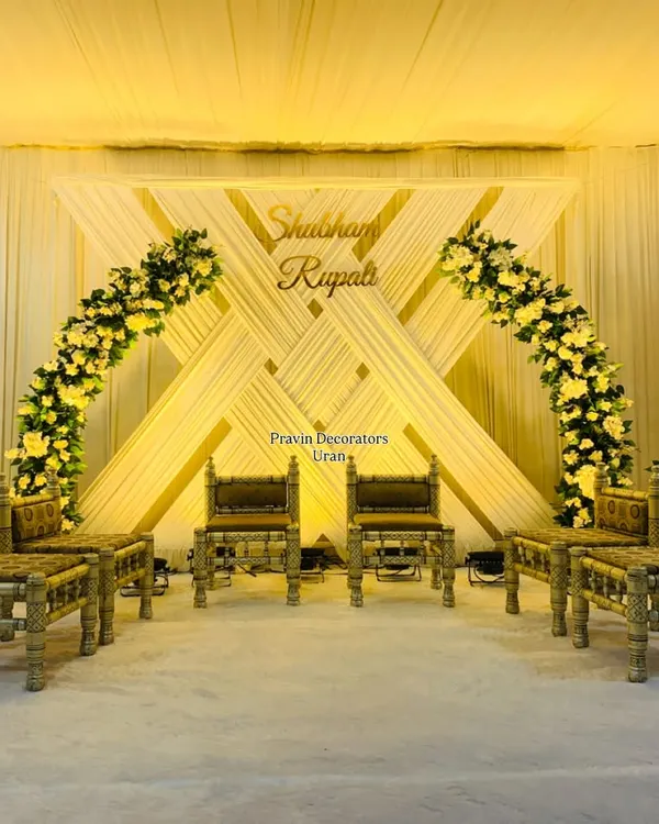This engagement stage features a unique backdrop of crisscrossing white drapes and warm gold accents. The design is completed with two beautiful arches of yellow flowers and traditional bajot-style seating for the couple.