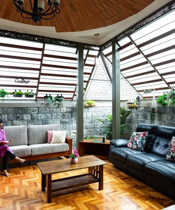 The living area in the Pioneer Lake residence is designed to feel like a sunroom. The slatted skylight roof floods the room with diffused natural light, highlighting the herringbone pattern of the reclaimed wood floor and the texture of the natural stone wall.