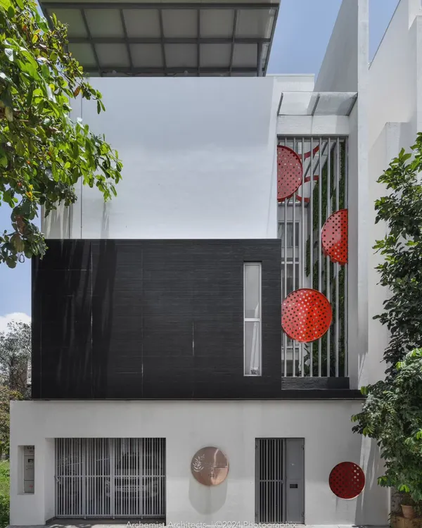 The elevation of Dr. Harsha's home reflects its minimal interior, with a monochromatic theme punctuated by a pop of red. The design features a prominent black stone-clad section and a triple-height courtyard screen.