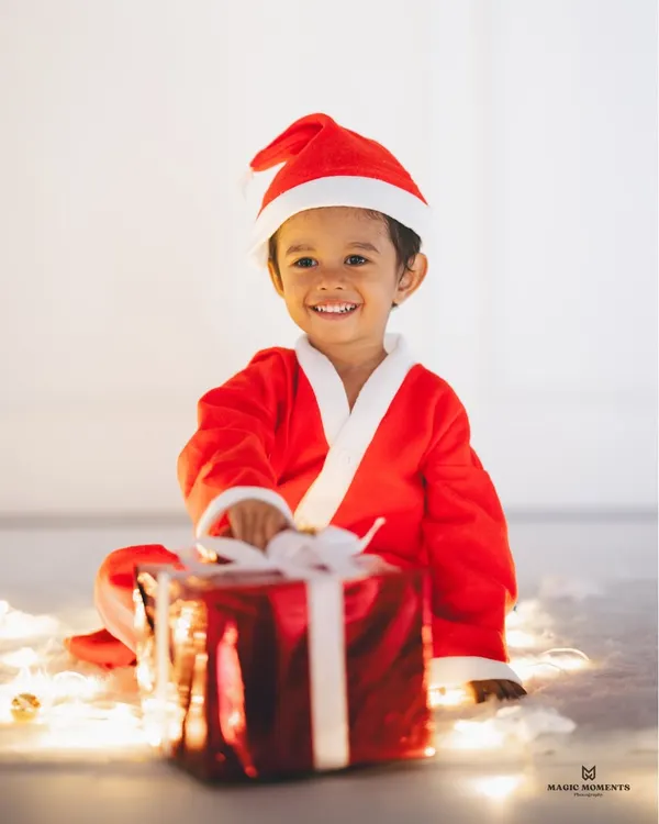 Capturing the pure joy of the season. This little one's bright smile is lit by the warm glow of Christmas lights during a festive studio session, creating a truly magical portrait.