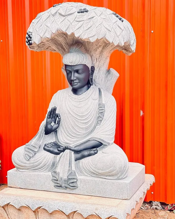 An intricately carved Buddha statue sitting under a stone Bodhi tree. This is a high-quality statement piece for any garden.