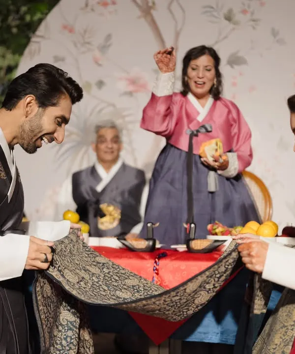 A joyful moment from a Korean Paebaek ceremony I planned, where the couple uses a cloth to catch dates and chestnuts thrown by their elders, symbolizing blessings for a fruitful life.