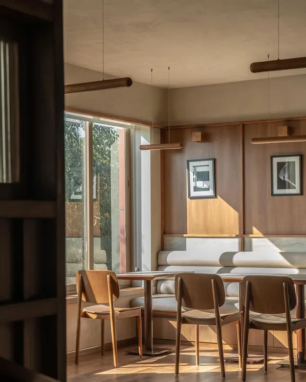 A sunlit corner in QBF Coffee, where the Japandi aesthetic comes to life. The warm wood paneling, clean lines of the furniture, and soft, natural light create a tranquil and inviting atmosphere, perfect for a quiet coffee or focused work.