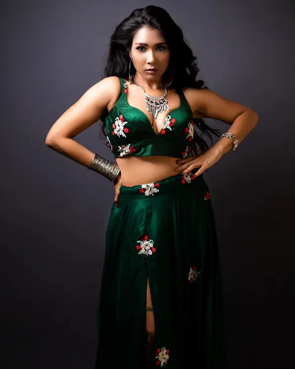 A full-length view of a custom green lehenga set. This modern ethnic piece features a deep-V crop top and a matching skirt with red and white floral embroidery, paired with bold silver jewelry.