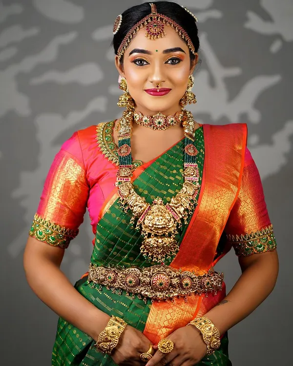 A complete South Indian bridal look featuring a green and orange Kanjeevaram saree. The makeup is designed to be waterproof and long-lasting, complementing the heavy temple jewellery.