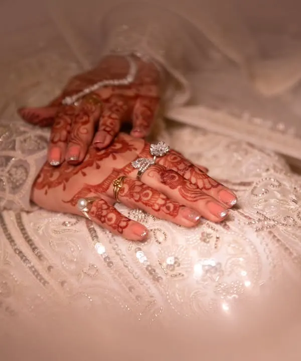 A close-up of the bride's hands, adorned with intricate mehndi and sparkling rings, resting on her embellished gown. These details are a beautiful part of her story.