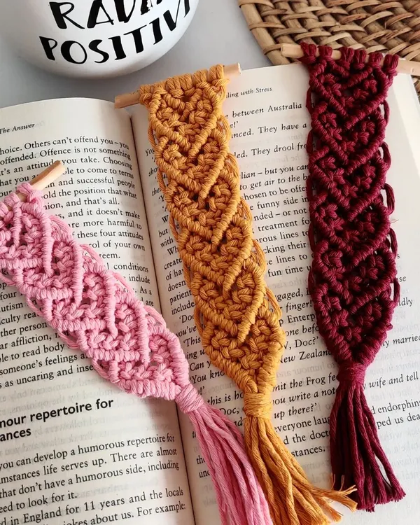 My heart pattern macrame bookmarks, available in pink, mustard, and maroon. These are attached to a small wooden dowel and have a tassel at the end.