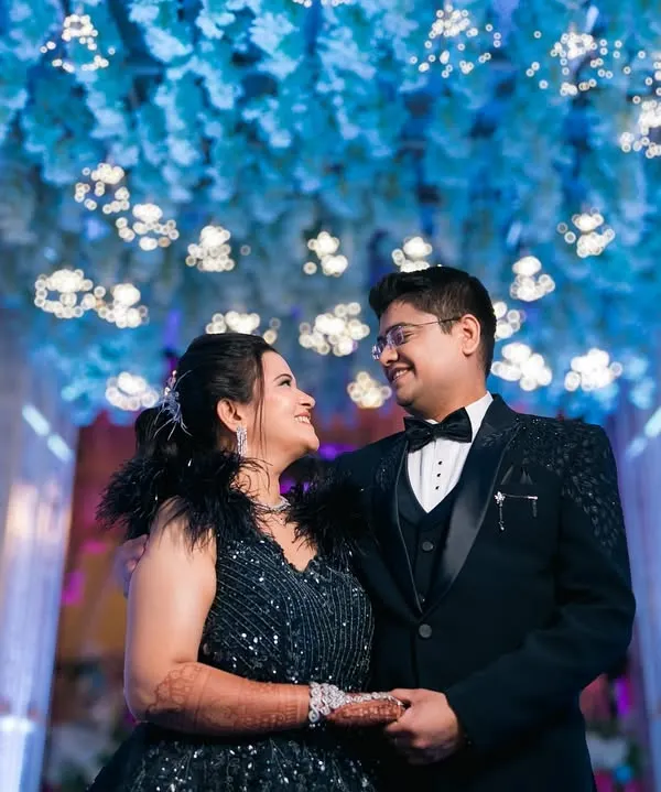 A glamorous engagement portrait with a modern fairytale feel. The couple looks stunning in their formal wear under a ceiling of blue flowers and lights.