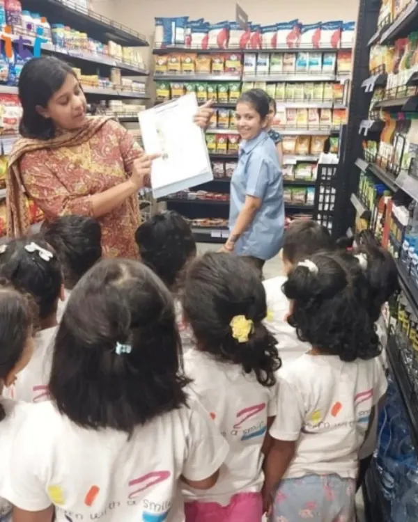A teacher explains a shopping list to children during a field trip to the supermarket. This real-world experience teaches them about planning, budgeting, and community helpers.