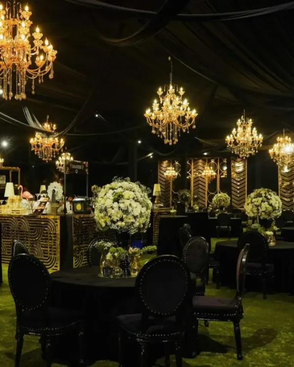A luxurious black-themed cocktail party setup. The decor features black tablecloths, grand crystal chandeliers, and large white floral centerpieces, creating a bold and sophisticated ambiance.