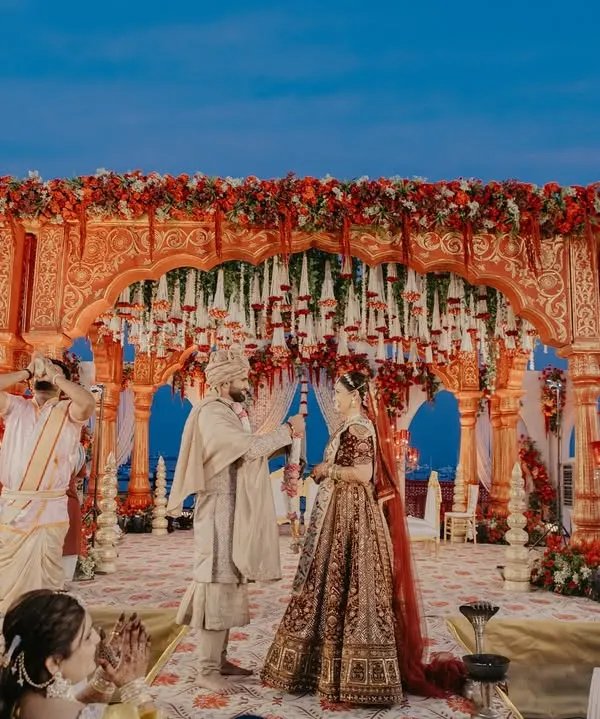 The Varmala ceremony under a magnificent floral mandap. We capture the entire scene to showcase the grandeur of the setup and the joy of the moment.