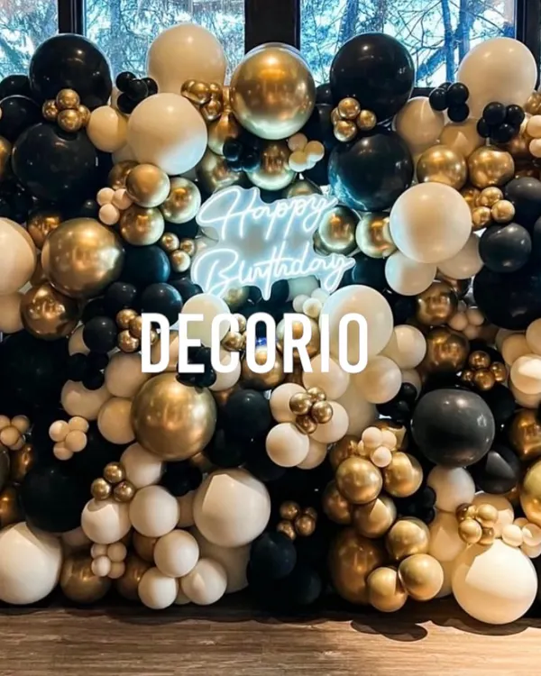 A stunning balloon wall in black, white, and chrome gold, creating a dense and luxurious backdrop. A 'Happy Birthday' neon sign is nestled within the balloons, adding a modern, glowing touch.