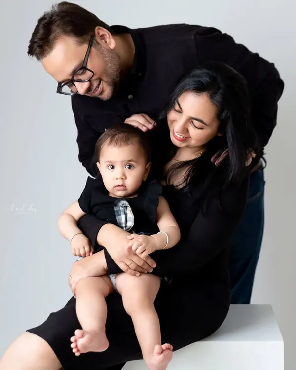 A loving family portrait with both parents smiling down at their baby, who is held securely in her mother's lap.