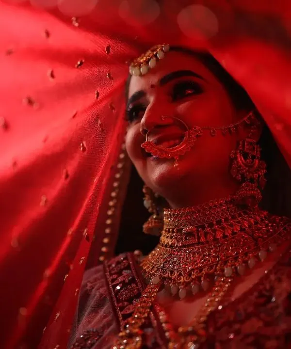 A bride's smile is her most beautiful accessory. Here, she is captured under her veil, with a makeup look centered on a classic red lip and glowing skin that radiates pure joy and confidence.