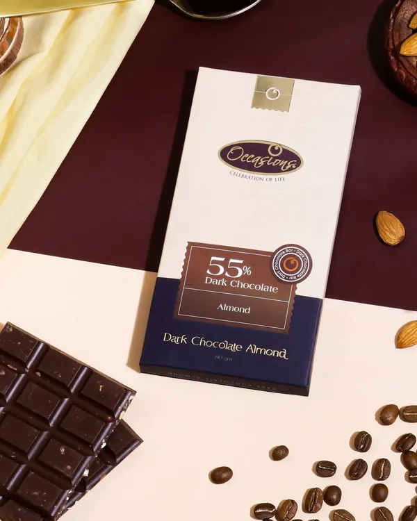 A stylish flat lay of a dark chocolate bar, composed with coffee beans, almonds, and contrasting colored backgrounds to tell a story of rich, complex flavors.