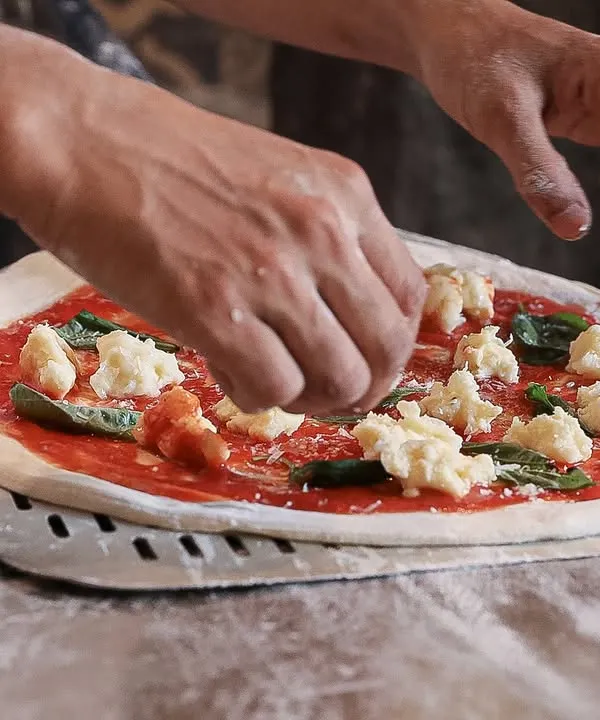 The making of a classic Margherita. Our pizzaiolo carefully places dollops of our fresh, handmade mozzarella on a base of rich tomato sauce and basil. It's an art form.
