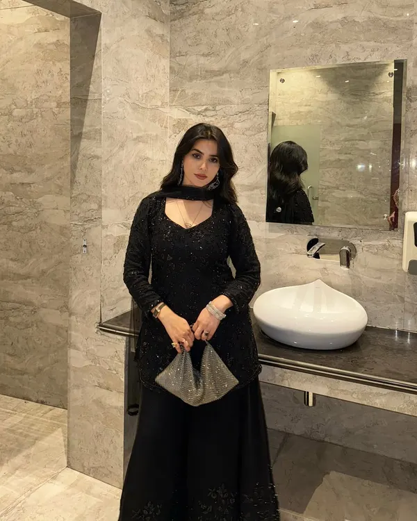 This is a full-length shot of a stunning black sequined ethnic outfit. The luxurious marble background of the washroom complements the outfit's elegance, making it perfect for showcasing high-end party wear.