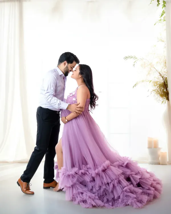 A romantic moment between expecting parents in a light and airy studio setting. The mother-to-be wears a stunning lilac ruffled gown, creating a soft and elegant maternity portrait.