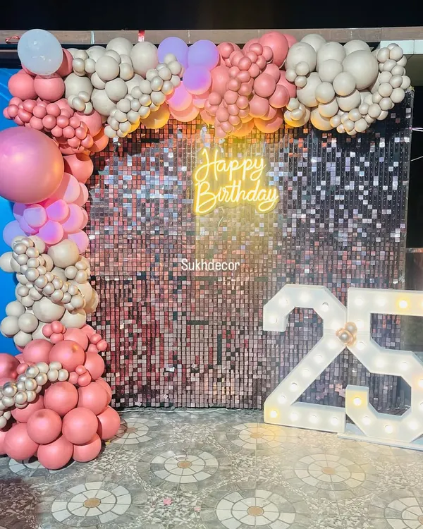 This 25th birthday setup is the definition of glam. The rose gold shimmer wall provides a sparkling backdrop for the organic balloon arch, neon sign, and large '25' marquee numbers.