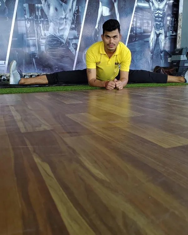Holding a front split on the gym floor. This level of flexibility is achievable with dedicated practice and proper guidance.