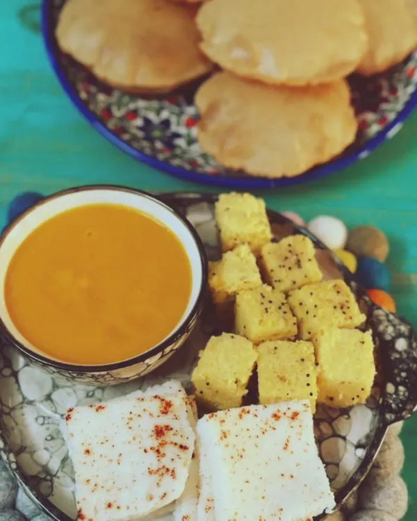 A perfect homemade Gujarati meal featuring sweet Aam Raas (mango pulp), fluffy puris, and savory white and yellow dhokla. This is the taste of summer and comfort, made fresh in our kitchen.