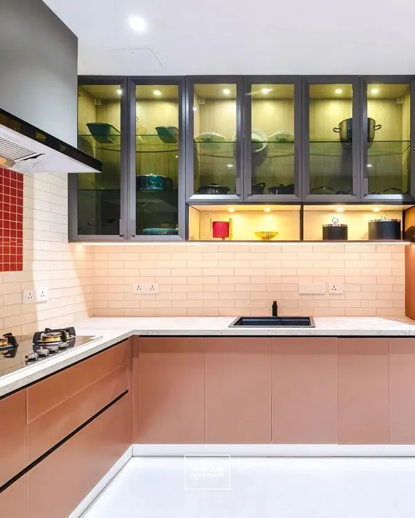 A sophisticated kitchen featuring rose-gold colored cabinets, a red mosaic tile backsplash, and glass-fronted upper cabinets with internal lighting. The built-in oven and microwave unit ensures a seamless look.