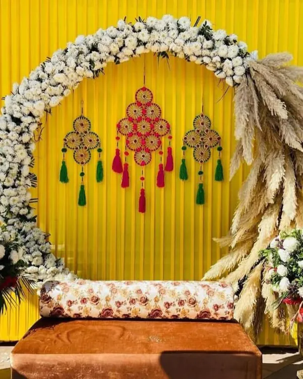A modern Mehndi or Haldi seating arrangement with a semi-circular arch of white flowers and pampas grass. We combined this with traditional hangings against a bright yellow backdrop to create a unique fusion look for a wedding function.