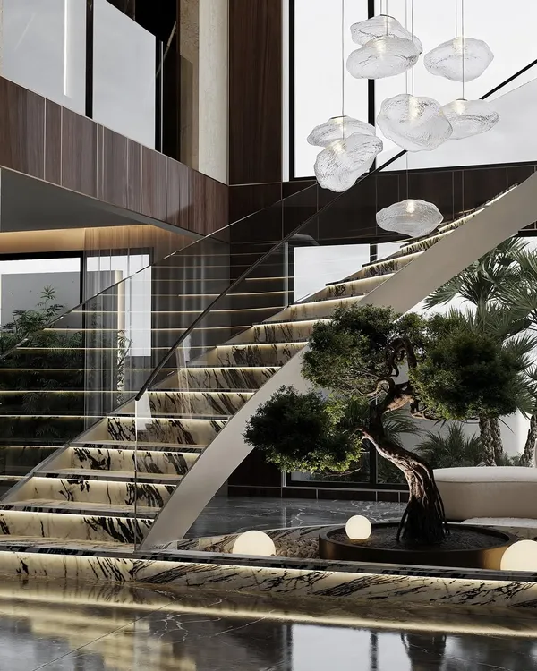 A luxurious double-height foyer featuring a curved staircase with marble steps and integrated lighting. A bonsai tree and an indoor water feature at the base create a serene and grand entrance.