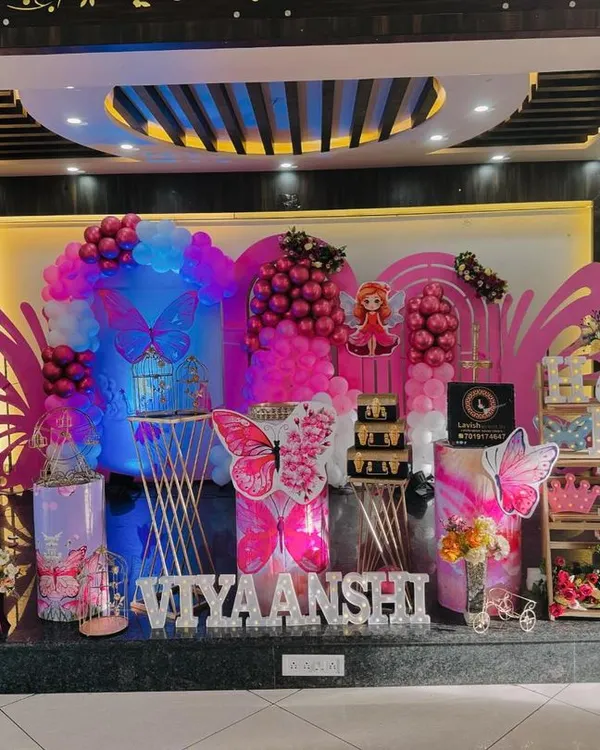 A full stage view of a vibrant butterfly-themed birthday party for 'Viyaanshi'. The setup includes large wing props, balloon columns, and personalized cutouts, creating an immersive experience.