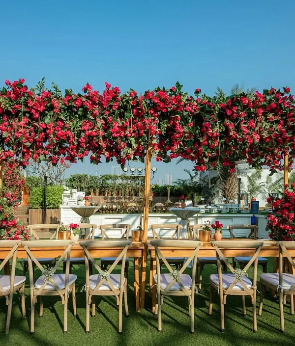 A spectacular outdoor dining setup featuring a long table under a canopy overflowing with vibrant bougainvillea.