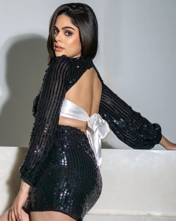 A stunning black sequined mini dress with a dramatic open back and a large white bow. This look is all about making a statement, combining classic glamour with a bold, modern twist.