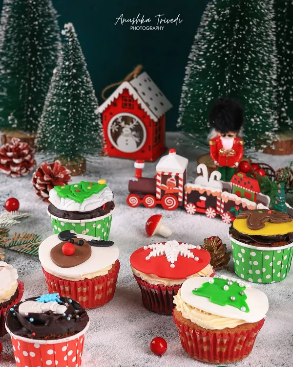 A whimsical Christmas scene with assorted cupcakes set amongst miniature trees and a toy train, creating a magical winter wonderland.