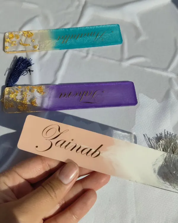 A set of three custom name bookmarks I made. Each one has a unique color combination, from teal and gold to purple and pink, with the name in a beautiful script.