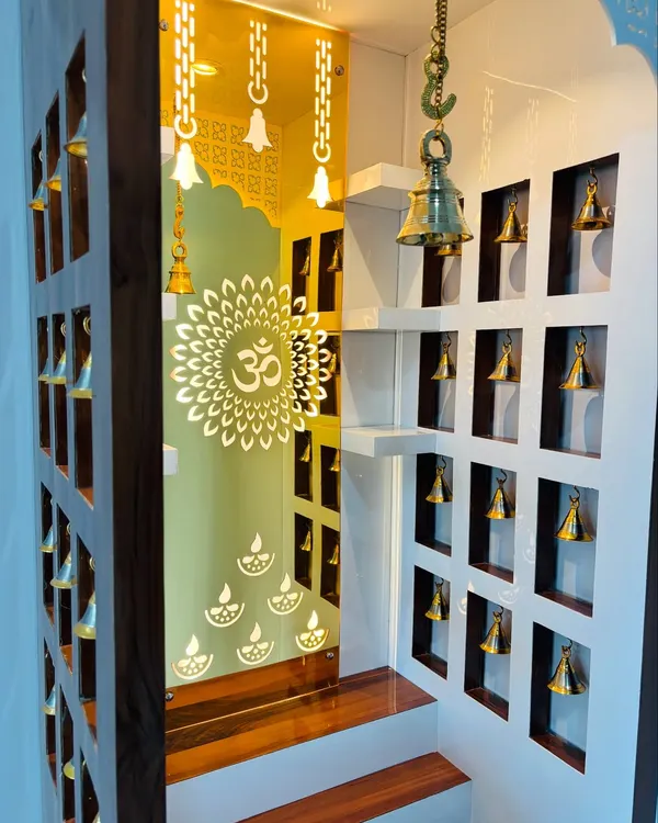 An interior view of a custom mandir, showcasing the beautiful backlit panel with an 'Om' mandala. The sides feature niches with small brass bells, creating a divine and peaceful ambiance.