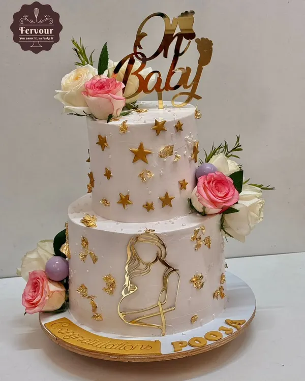 A beautiful two-tier baby shower cake with a "Oh Baby" theme. This cake is decorated with fresh flowers, gold stars, and an elegant silhouette of a mother-to-be.