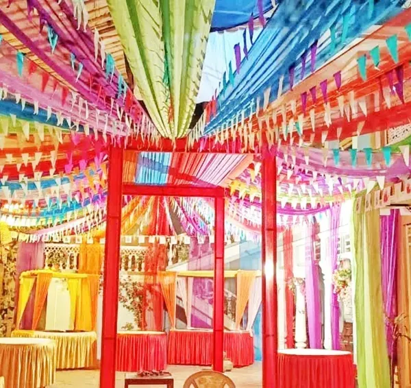 The interior of a colorful pandal designed for a festival celebration. The ceiling is covered with multi-colored fabric streamers and pennant banners, creating a joyful and energetic environment.