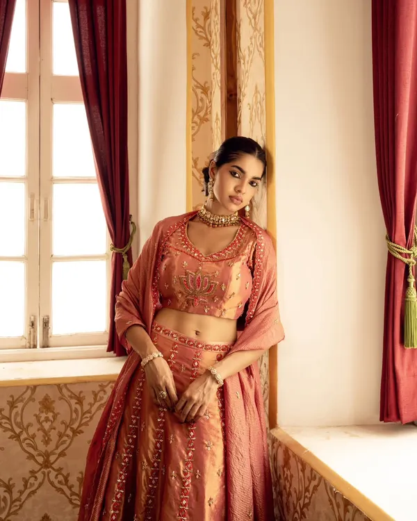 A soft, romantic portrait captured using natural window light. This image from a brand campaign highlights the delicate embroidery of the lehenga in a serene, elegant setting.