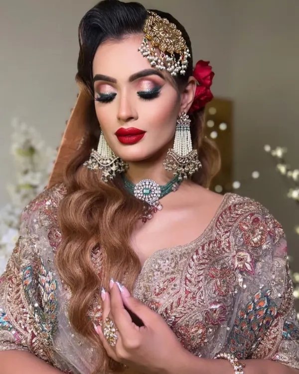 A glamorous Nikkah look featuring bold red lips and dramatic eyes. The side-swept Hollywood waves and a statement passa complete this advanced bridal makeup style.