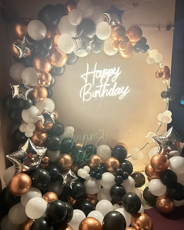 A full and luxurious balloon arch in black, white, and rose gold, with a neon sign creating a glamorous photo corner.