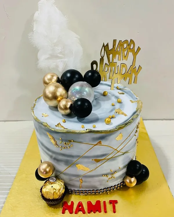A cool and contemporary cake with a grey marble effect, accented with black and gold spheres, gold leaf, and a white feather. Perfect for a stylish celebration.