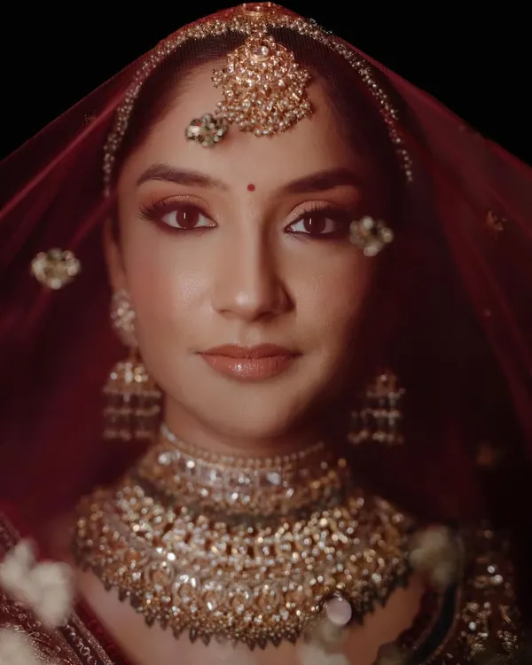 A classic bridal portrait. The direct gaze, rich colors of the red veil, and intricate jewelry come together to create a powerful and timeless image of the bride, Diksha.